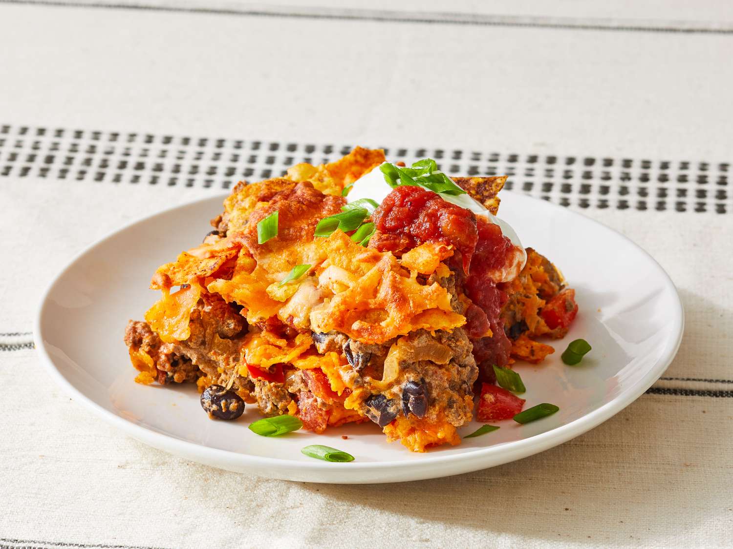 Ingredients for Dorito casserole arranged on a kitchen counter, including ground beef, Doritos, shredded cheddar, sour cream, salsa, beans, and taco seasoning
