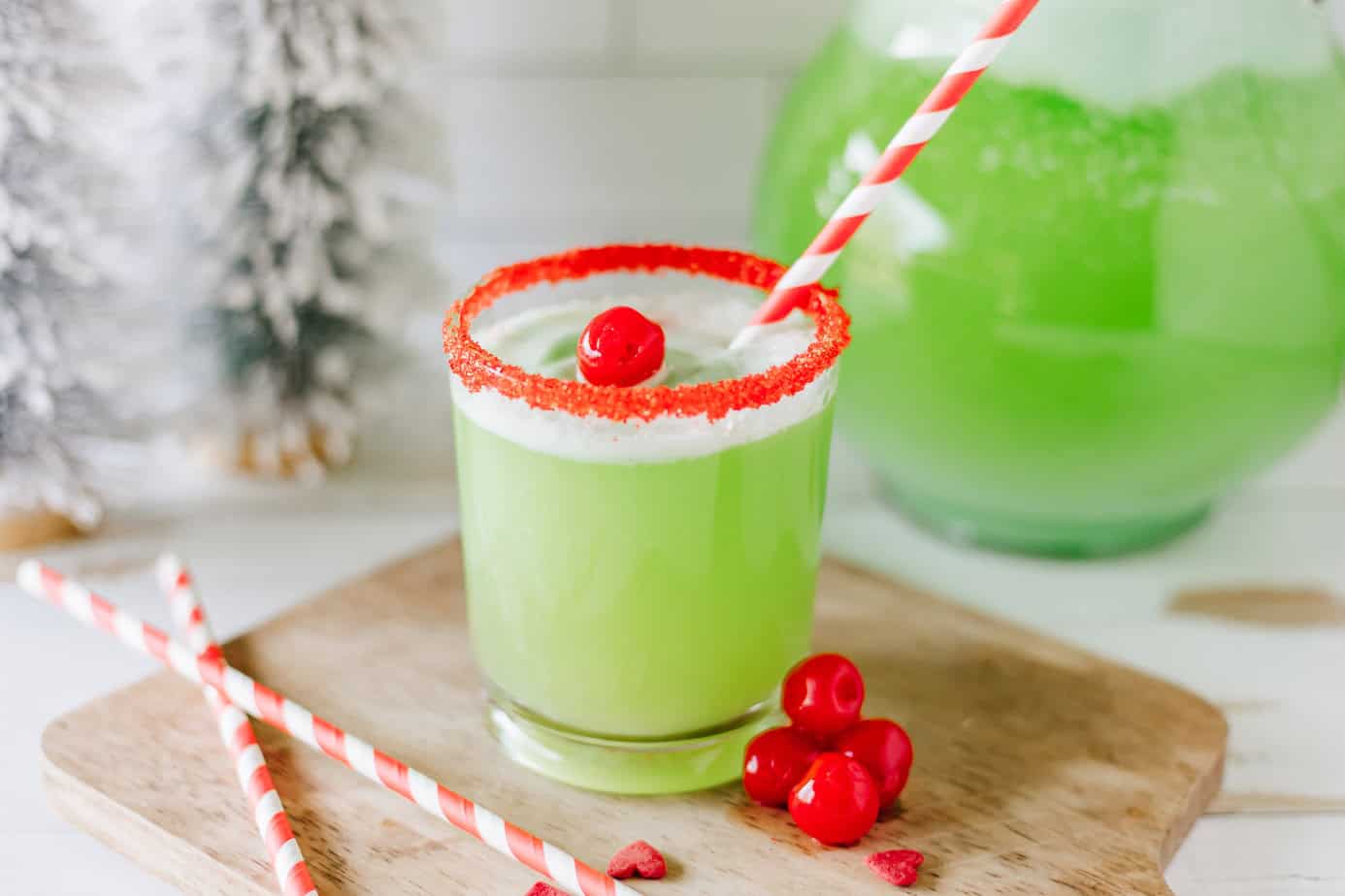 Ingredients for Grinch punch arranged on a kitchen counter including lime sherbet, lemon-lime soda, pineapple juice, and clear cups, with a large punch bowl in the background