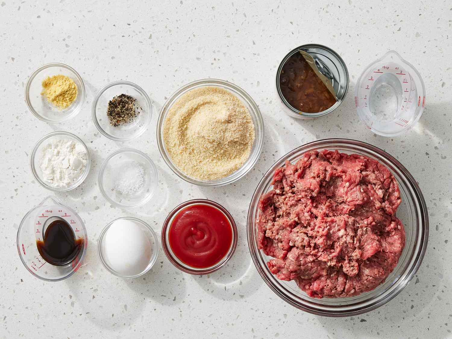 Ingredients for Salisbury steak on a kitchen counter, including ground beef, onion, mushrooms, breadcrumbs, egg, beef broth, Worcestershire sauce, and seasonings