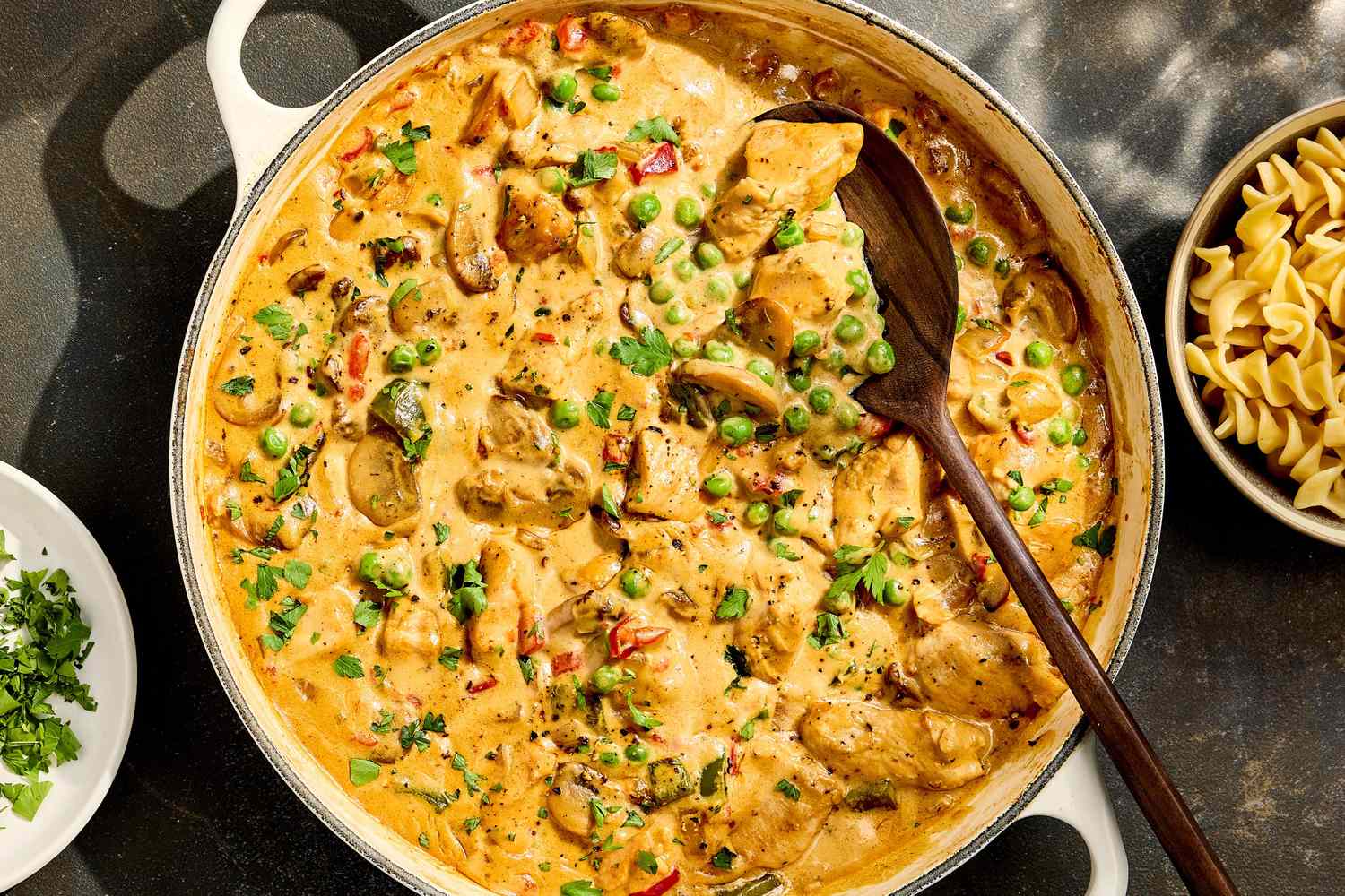Ingredients for chicken à la king arranged on a kitchen counter including cooked chicken, mushrooms, bell pepper, onion, peas, broth, cream, and spices