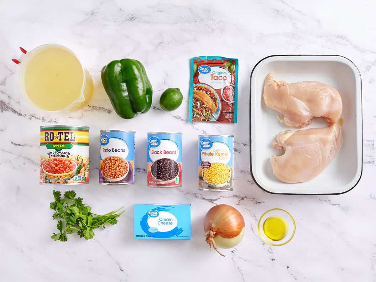Ingredients for chicken taco soup on a counter: canned beans, corn, salsa, chicken, broth, onion, garlic, spices, lime, and toppings