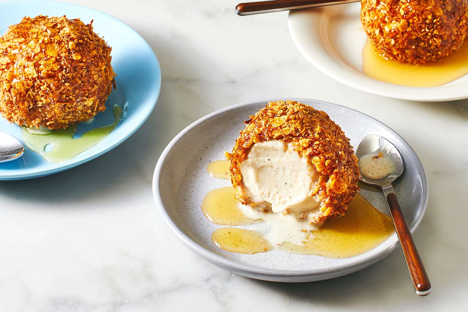 Ingredients for fried ice cream arranged on a kitchen counter including vanilla ice cream, cornflakes, cinnamon, sugar, eggs, flour, and oil