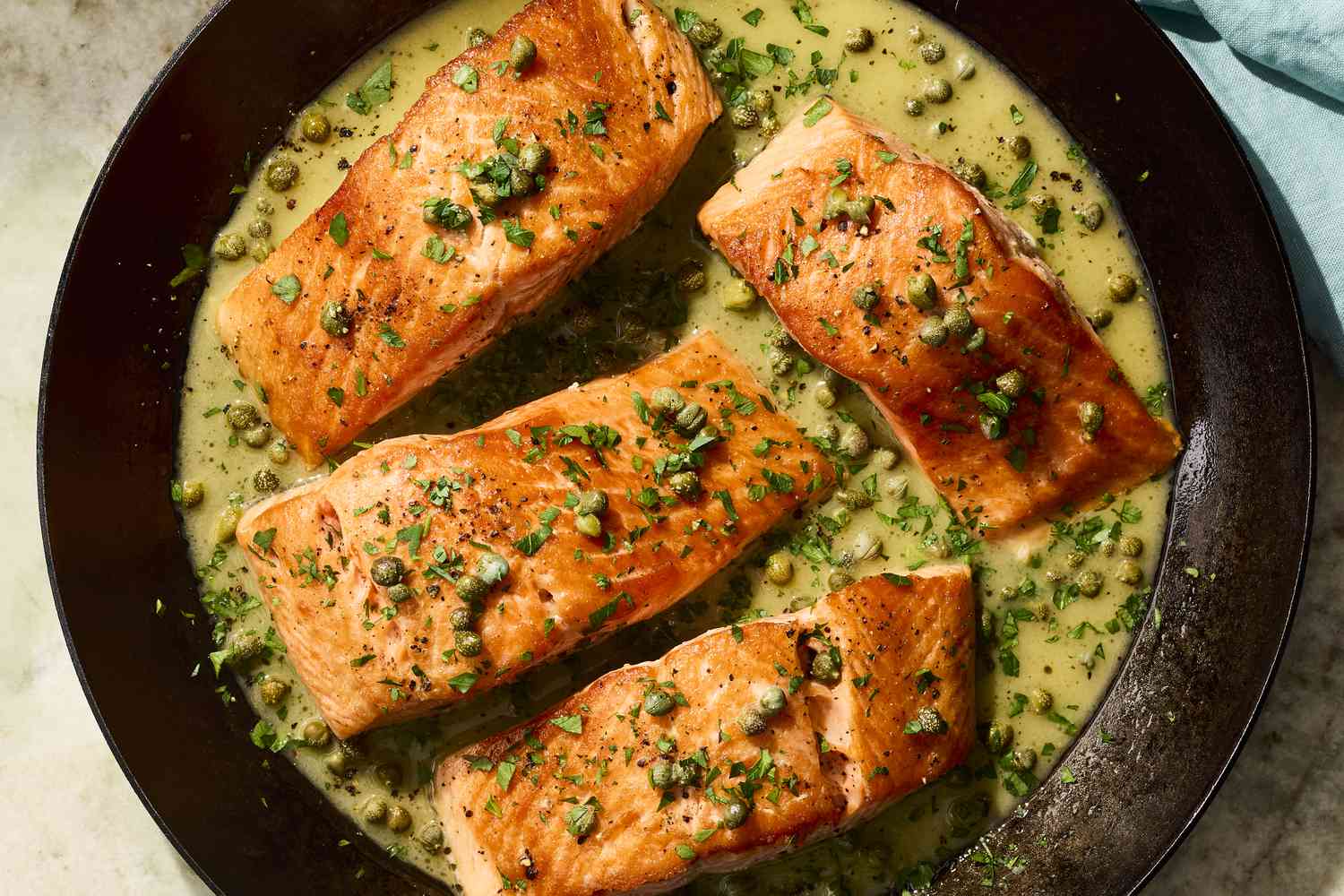 Ingredients for pan fried salmon and lemon butter caper sauce arranged on a kitchen counter: salmon fillets, lemon, capers, butter, garlic, parsley, salt, pepper, and oil in warm natural light
