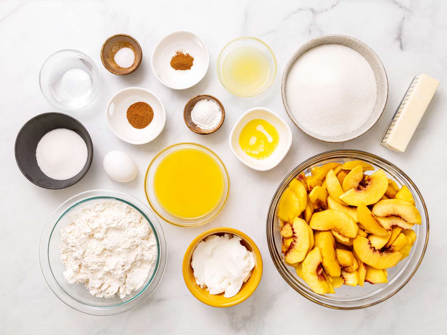 Ingredients for peach cobbler including canned peaches, Bisquick mix, sugar, cinnamon, milk, and butter arranged on a bright kitchen counter