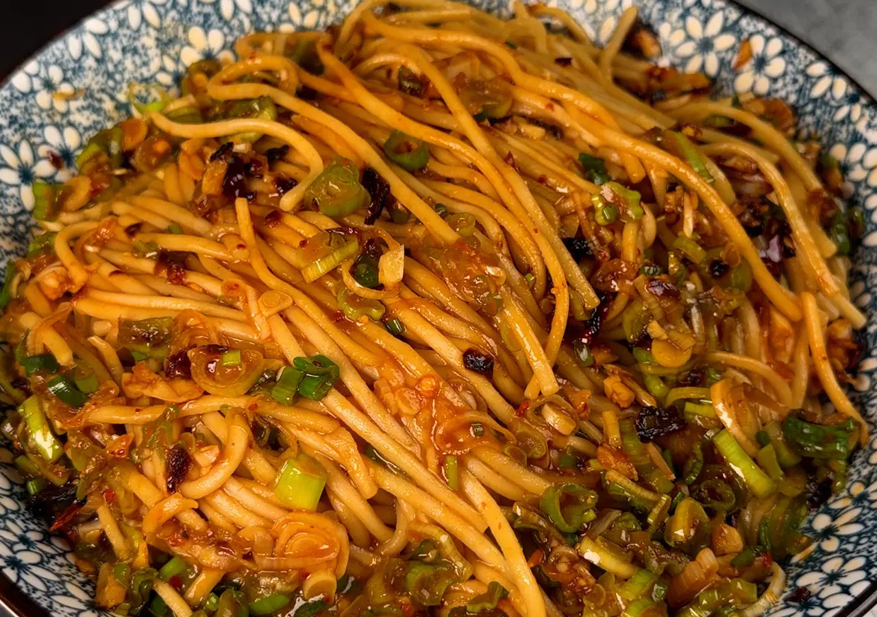 Ingredients for spicy garlic udon arranged on a kitchen counter including udon packs, soy sauce, chili crisp, garlic, scallions, sesame oil, and mixed vegetables