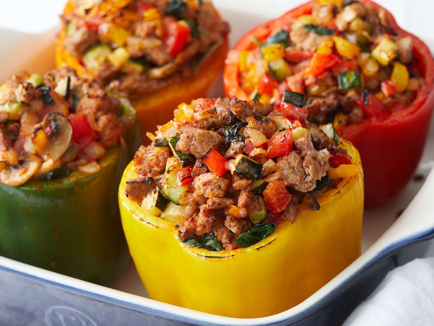 Ingredients for stuffed pepper filling arranged on a kitchen counter including bell peppers, ground beef, onion, garlic, tomatoes, rice, and seasonings