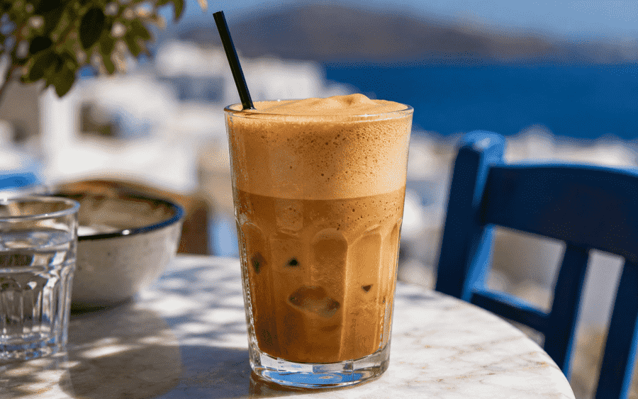 Instant coffee granules, sugar, ice cubes, and milk arranged in small bowls on a tidy kitchen counter with a glass and straw nearby