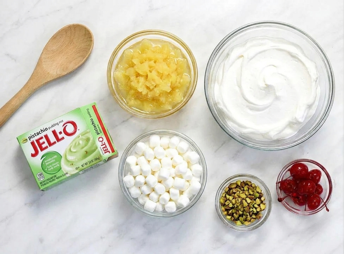 Instant pistachio pudding mix, crushed pineapple, whipped topping, mini marshmallows, chopped pistachios, and maraschino cherries arranged on a clean kitchen counter