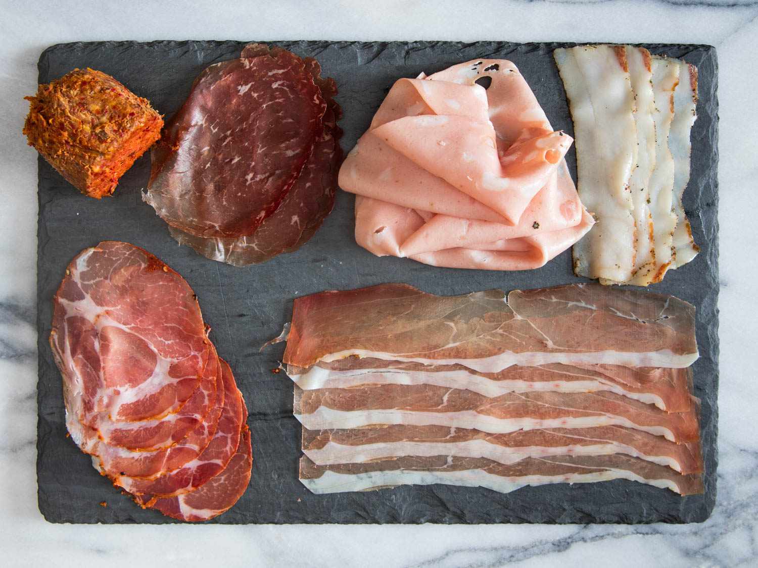 Italian deli meats, provolone, shredded lettuce, tomatoes, red onion, and pepperoncini arranged on a cutting board and counter for sandwich prep