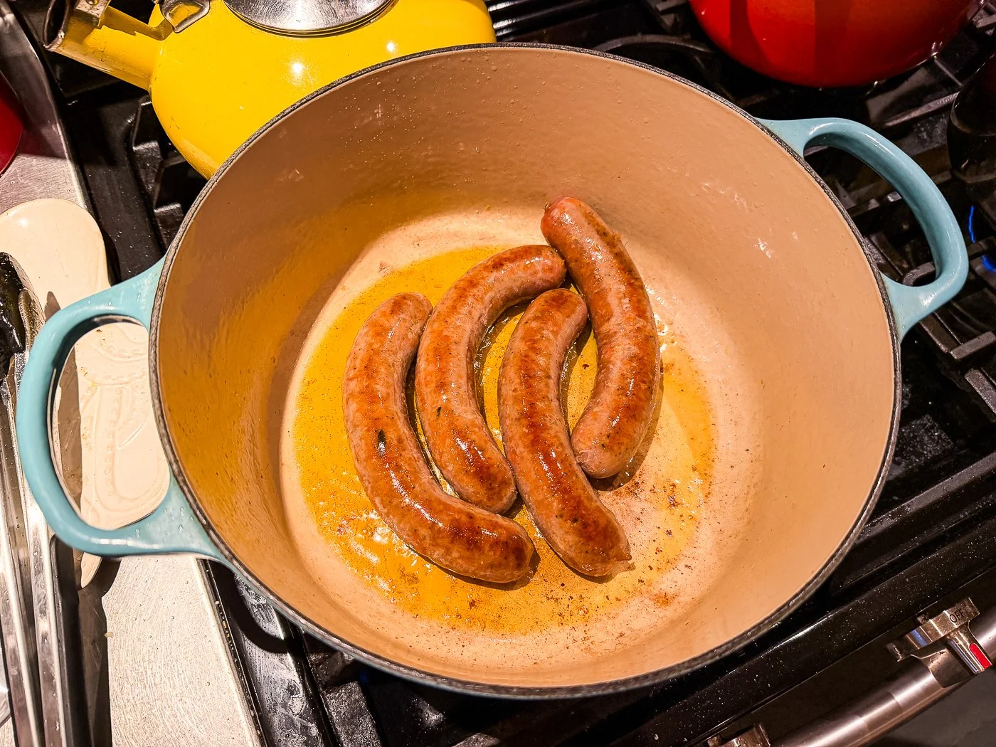 Italian sausage browning in a Dutch oven on a stovetop with a wooden spoon stirring