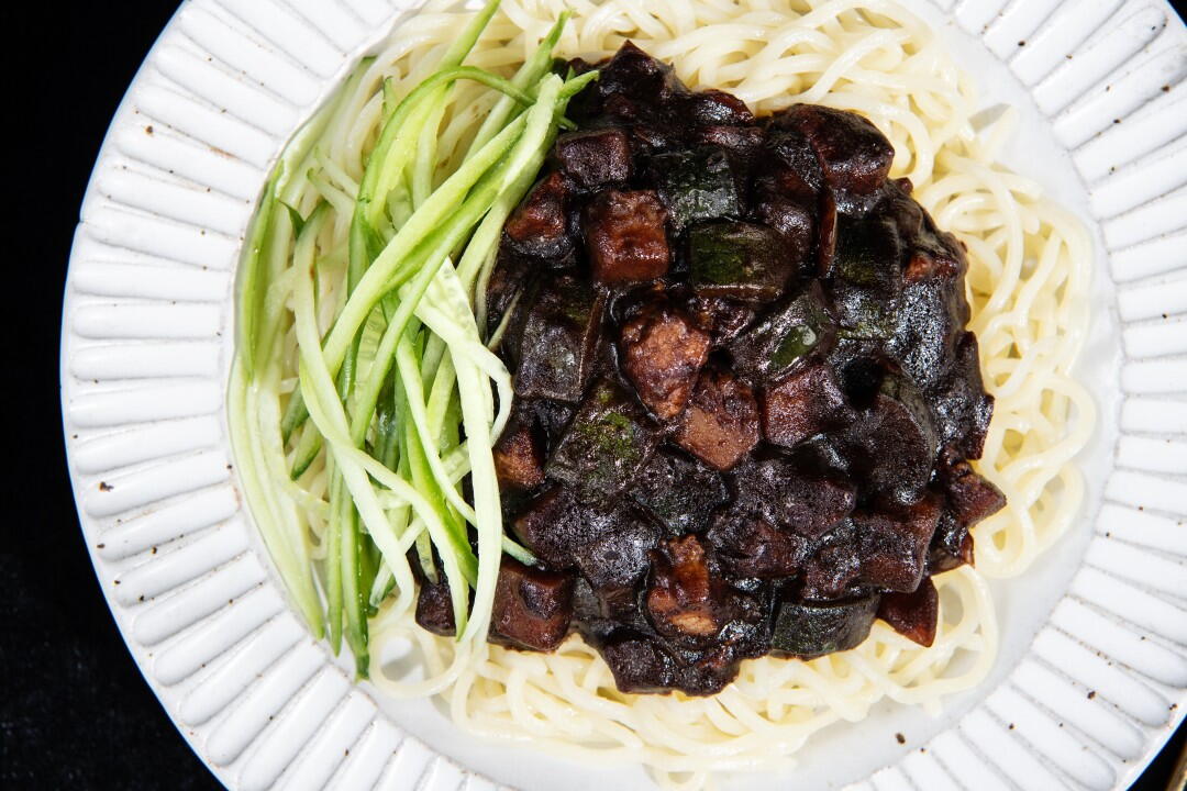 Jajangmyeon ingredients on a kitchen counter including chunjang black bean paste, fresh noodles, diced pork, onion, zucchini, potato, and cucumber