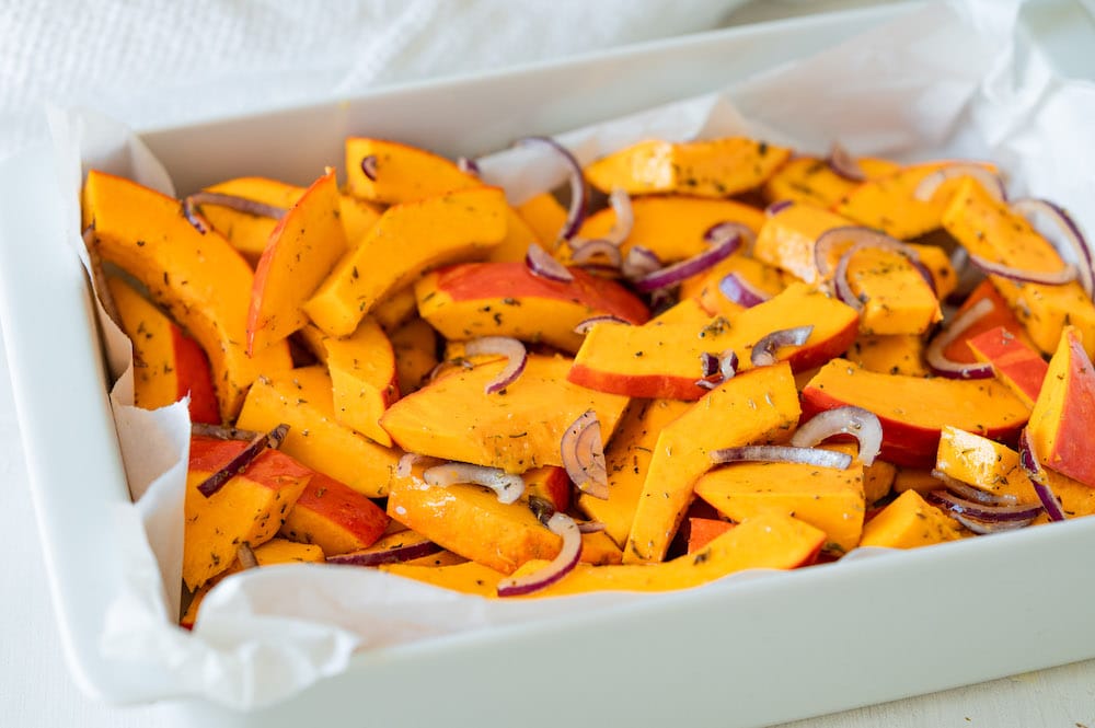 Kabocha squash cut into thick wedges on a wooden cutting board with seeds removed, in a bright home kitchen