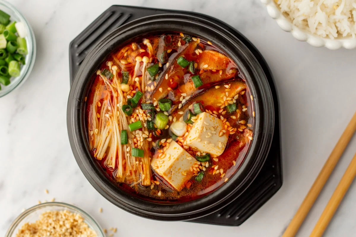 Kimchi, gochugaru, gochujang, and a package of extra-soft tofu arranged on a cutting board, ready for cooking