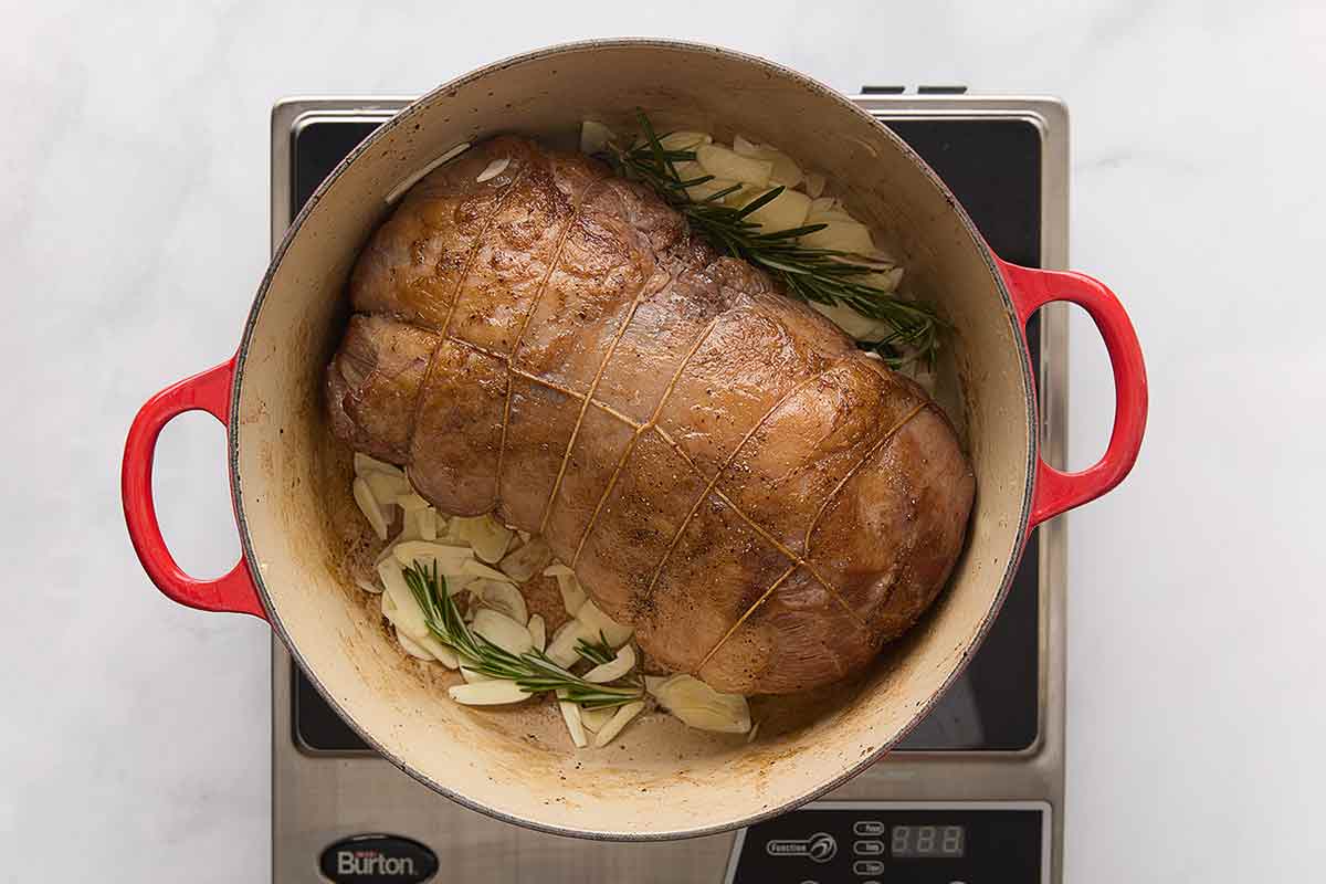 Lamb chunks browning in a Dutch oven with deep golden edges, steam rising over a stovetop