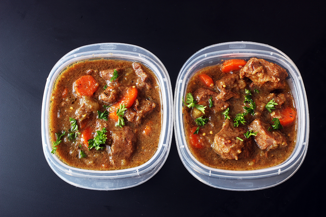 Leftover beef stew stored in a clear glass meal prep container with a lid on a kitchen counter
