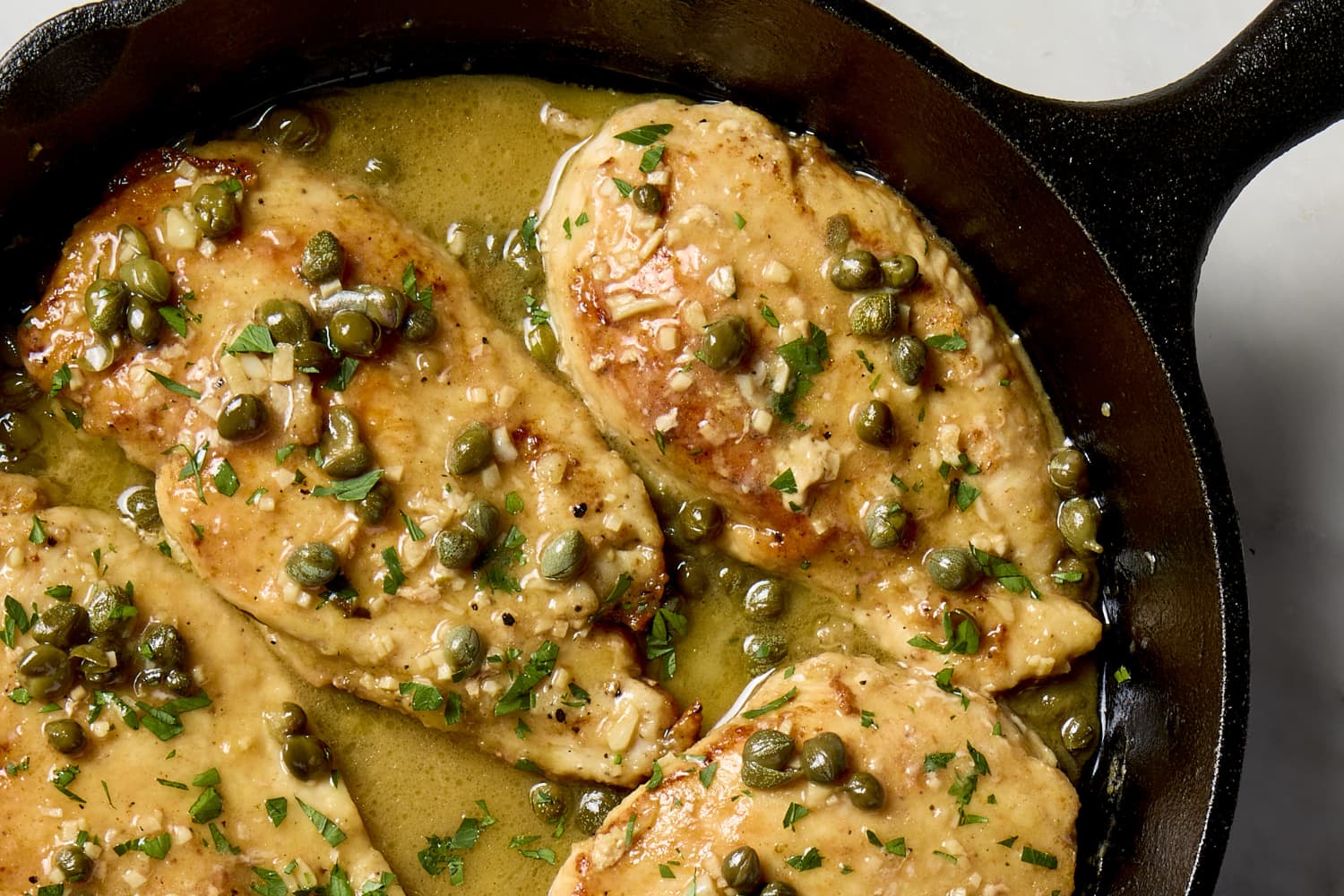 Lemon caper pan sauce simmering in a stainless steel skillet with browned bits being stirred with a wooden spoon on a stovetop