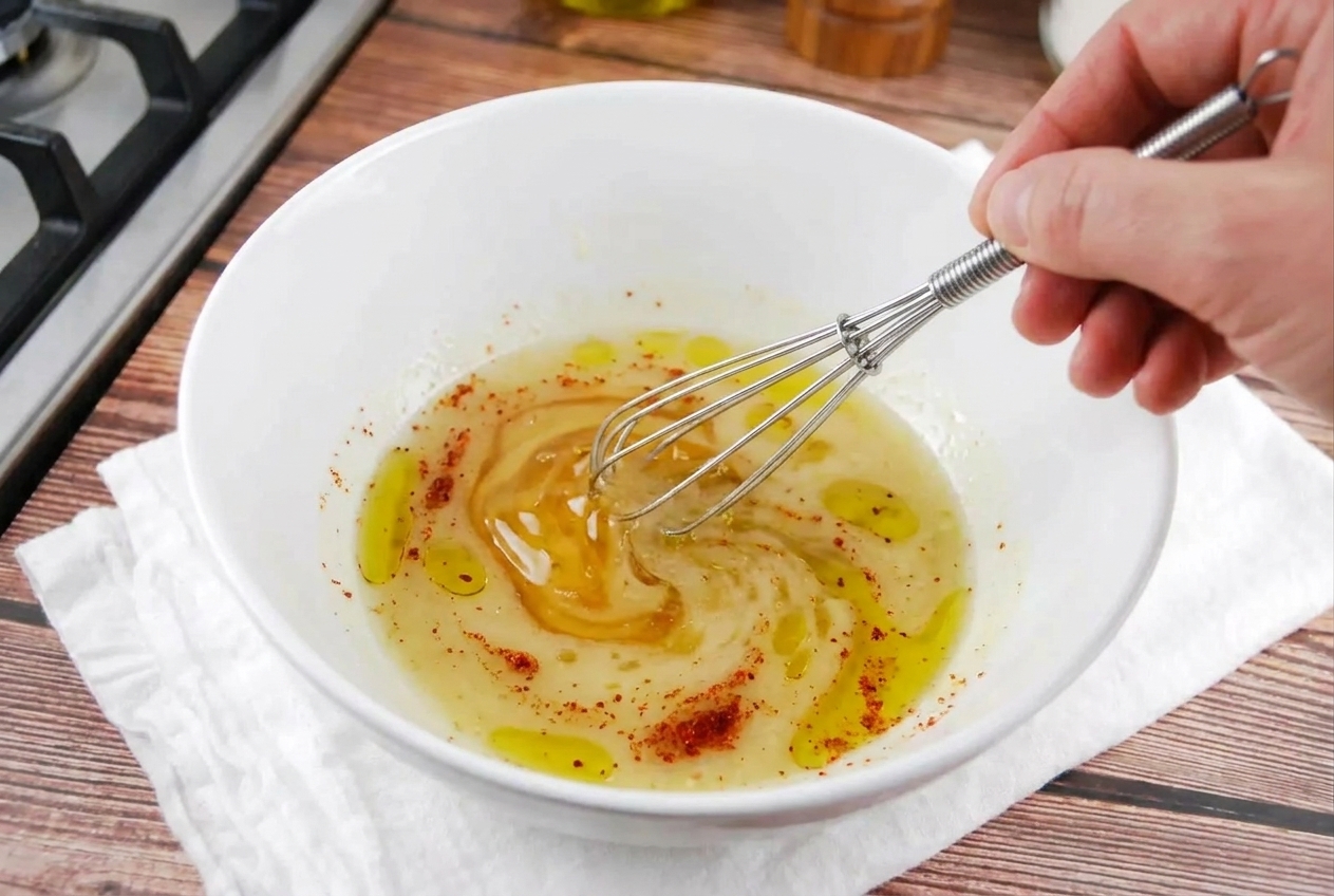 Lime juice, olive oil, chili powder, and honey being whisked together in a small bowl on a kitchen counter