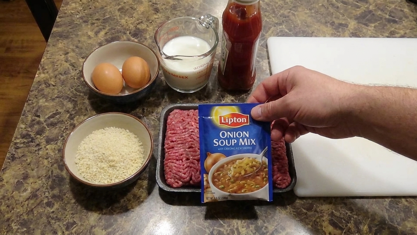 Lipton Onion Soup Mix packet alongside ground beef, eggs, breadcrumbs, ketchup, and milk arranged on a light kitchen counter