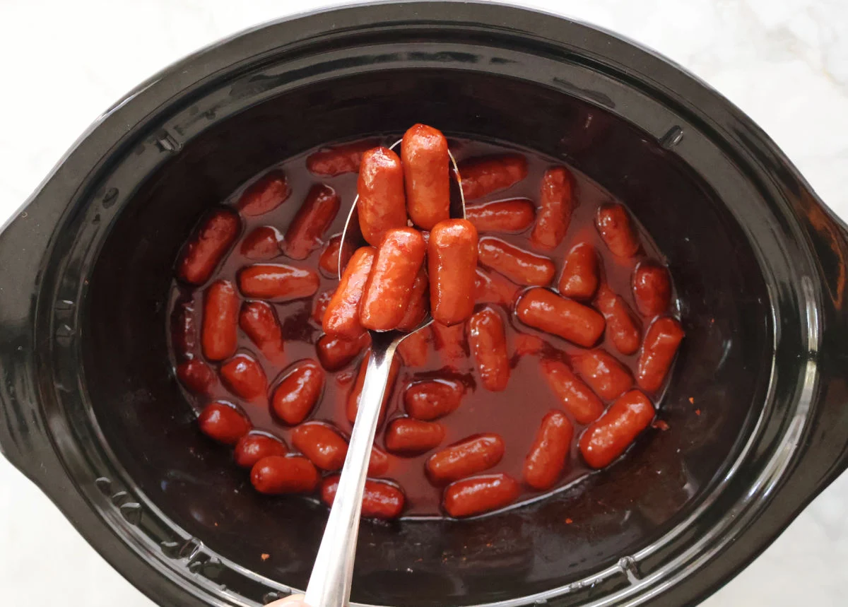Little smokies gently simmering in a thick barbecue and brown sugar sauce on a stovetop