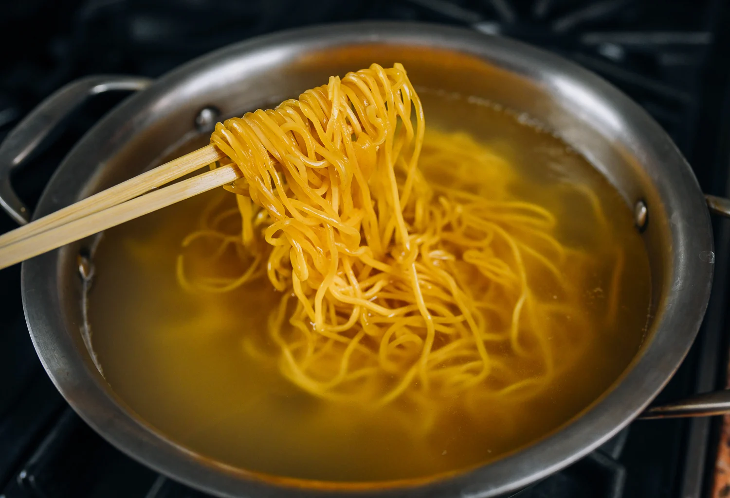 Lo mein noodles boiling in a pot of water on a stovetop with steam rising