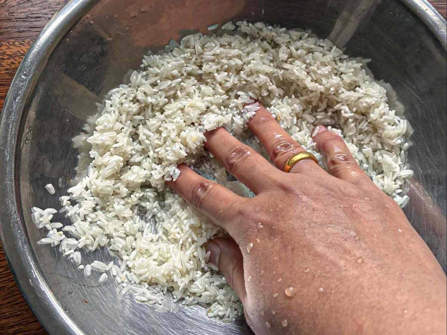 Long-grain white rice being rinsed in a fine-mesh strainer under running water in a home kitchen sink