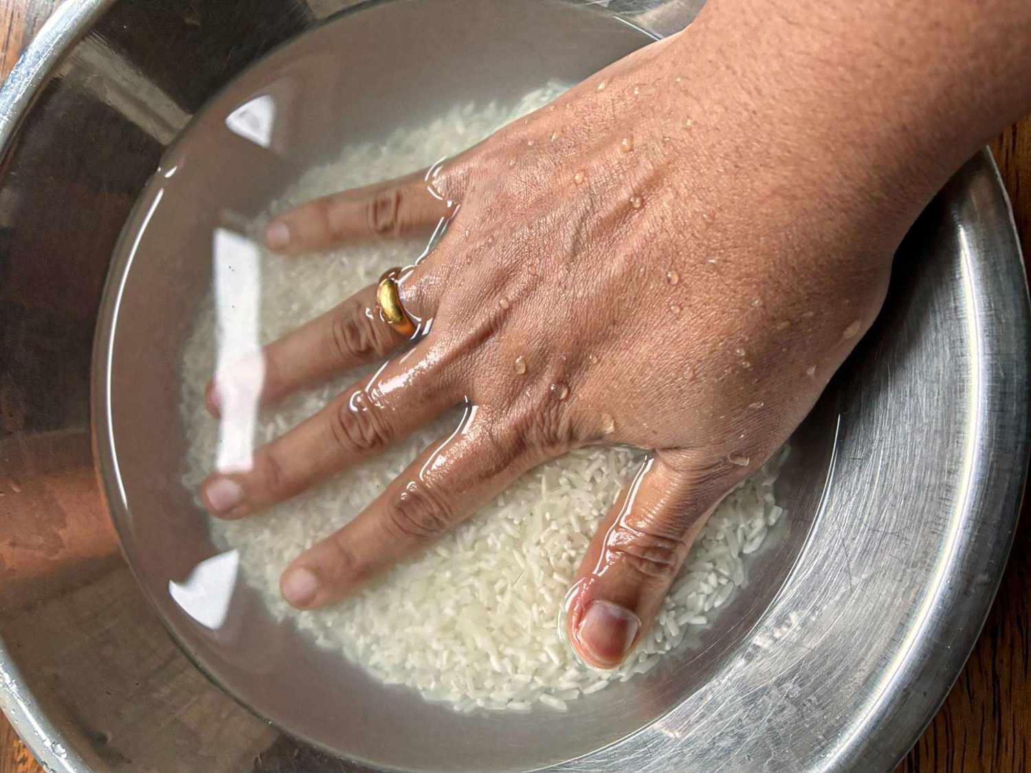 Long-grain white rice being rinsed in a fine-mesh strainer under running water over a sink