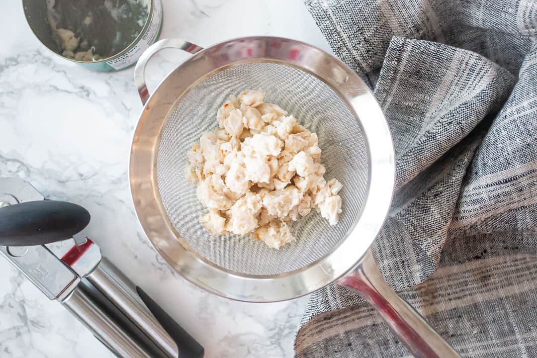 Lump crab meat sitting in a fine mesh strainer over a bowl on a kitchen counter, draining excess liquid before being added to dip