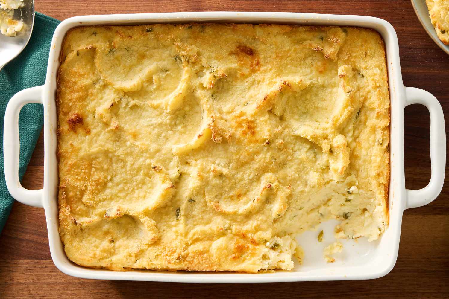 Mashed potatoes being spread over a baking dish filled with lentil vegetable filling using a spatula