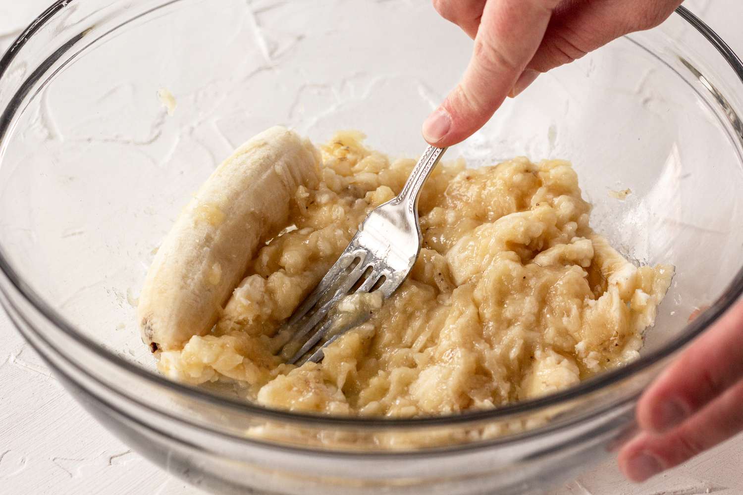 Mashed ripe bananas in a mixing bowl with a fork resting inside on a light kitchen counter