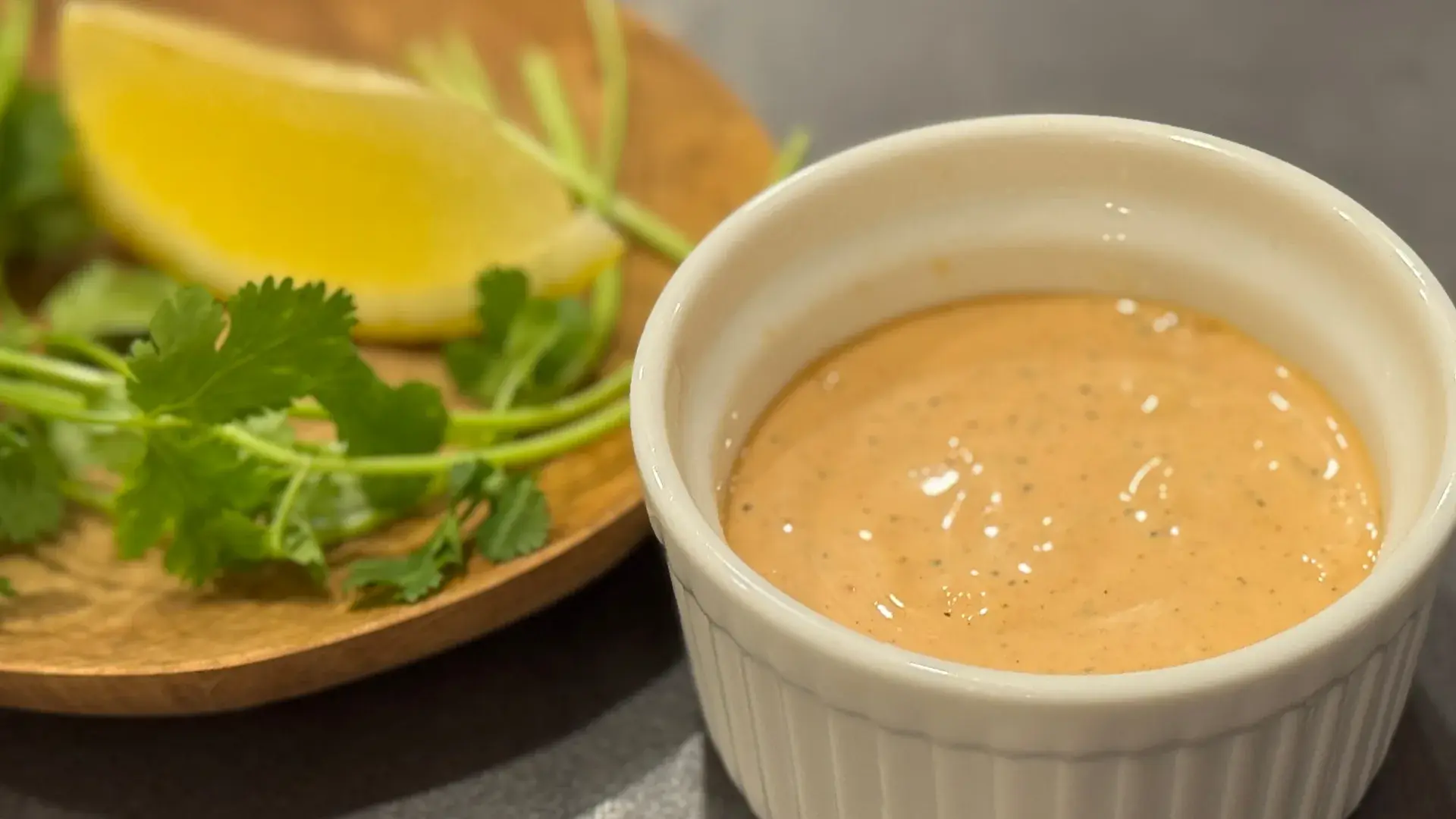 Mayonnaise, a lime half, peeled garlic clove, and chipotle peppers in adobo arranged as ingredients on a clean kitchen counter