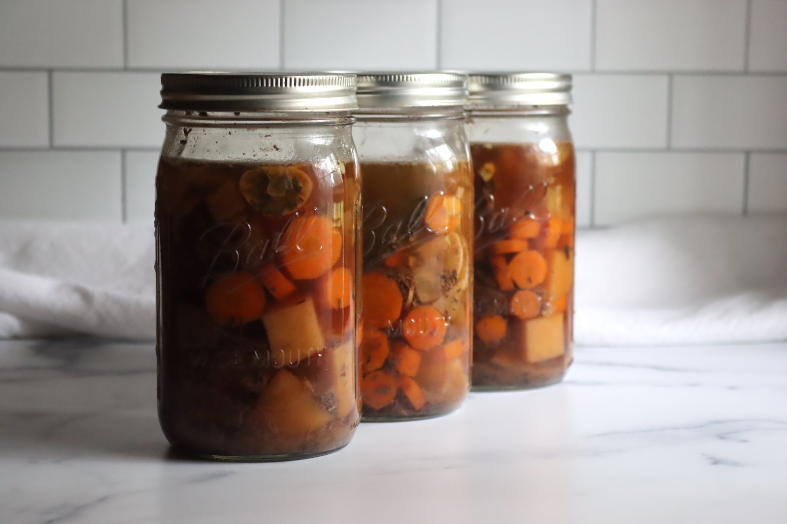 Meal prep containers filled with shredded pot roast, carrots, potatoes, and brown gravy on a kitchen counter ready for the refrigerator