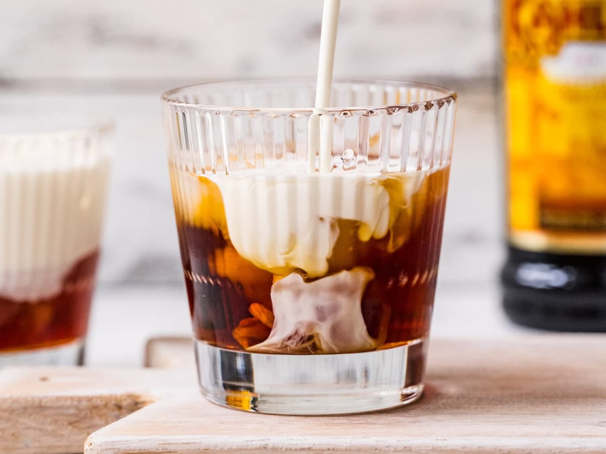 Measured Kahlua, vodka, and cream in small glass cups beside a rocks glass filled with large ice cubes on a home kitchen counter