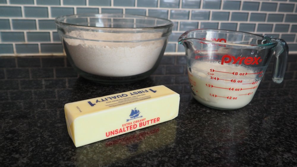 Measured flour, cocoa powder, sugar, baking powder, cold butter, buttermilk, and chocolate chips arranged on a clean kitchen counter
