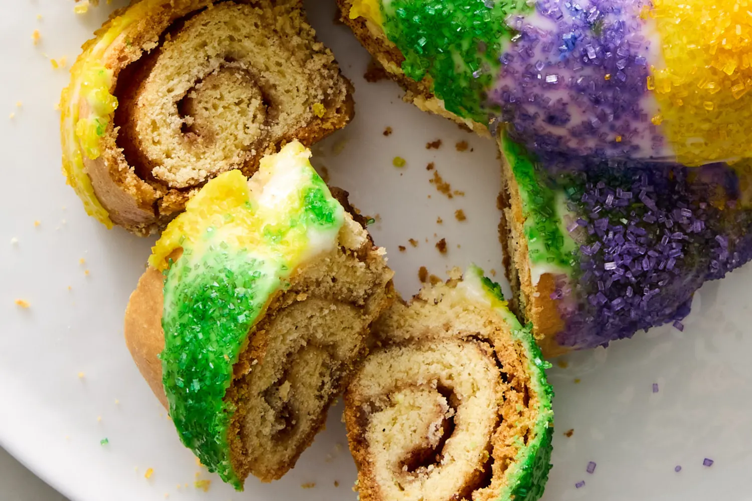 Measured flour, sugar, butter, eggs, yeast, milk, cinnamon, and bowls of purple, green, and gold sanding sugar arranged on a bright kitchen counter