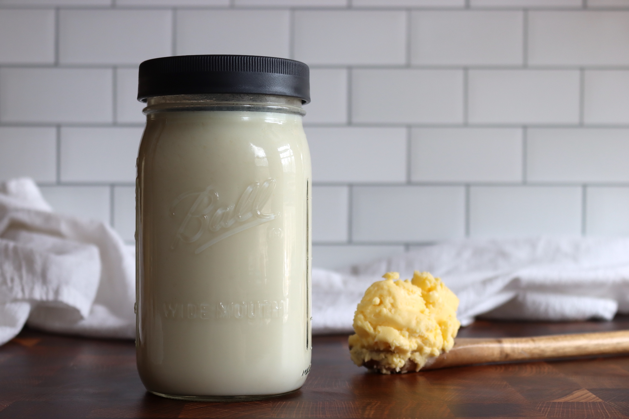 Measured heavy cream and cultured buttermilk on a light stone kitchen counter next to a clean jar and spoon, ready for mixing in soft natural light