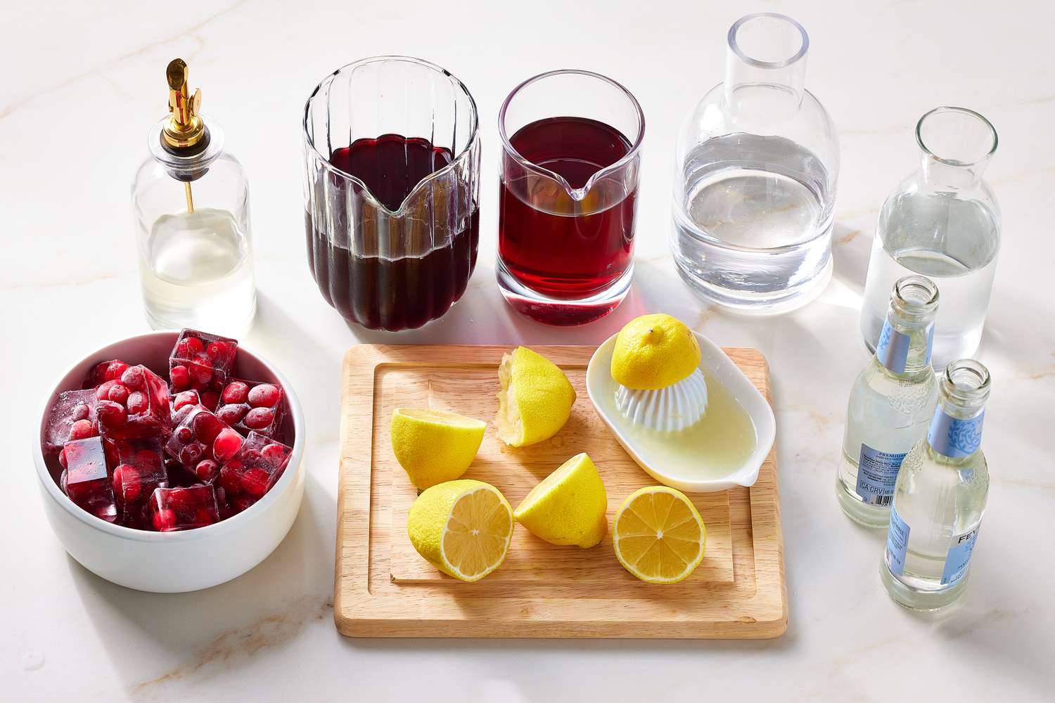 Measured ingredients for Christmas punch on a kitchen counter including cranberry juice, orange juice, ginger ale, sparkling wine, fresh oranges, limes, rosemary, and fresh cranberries