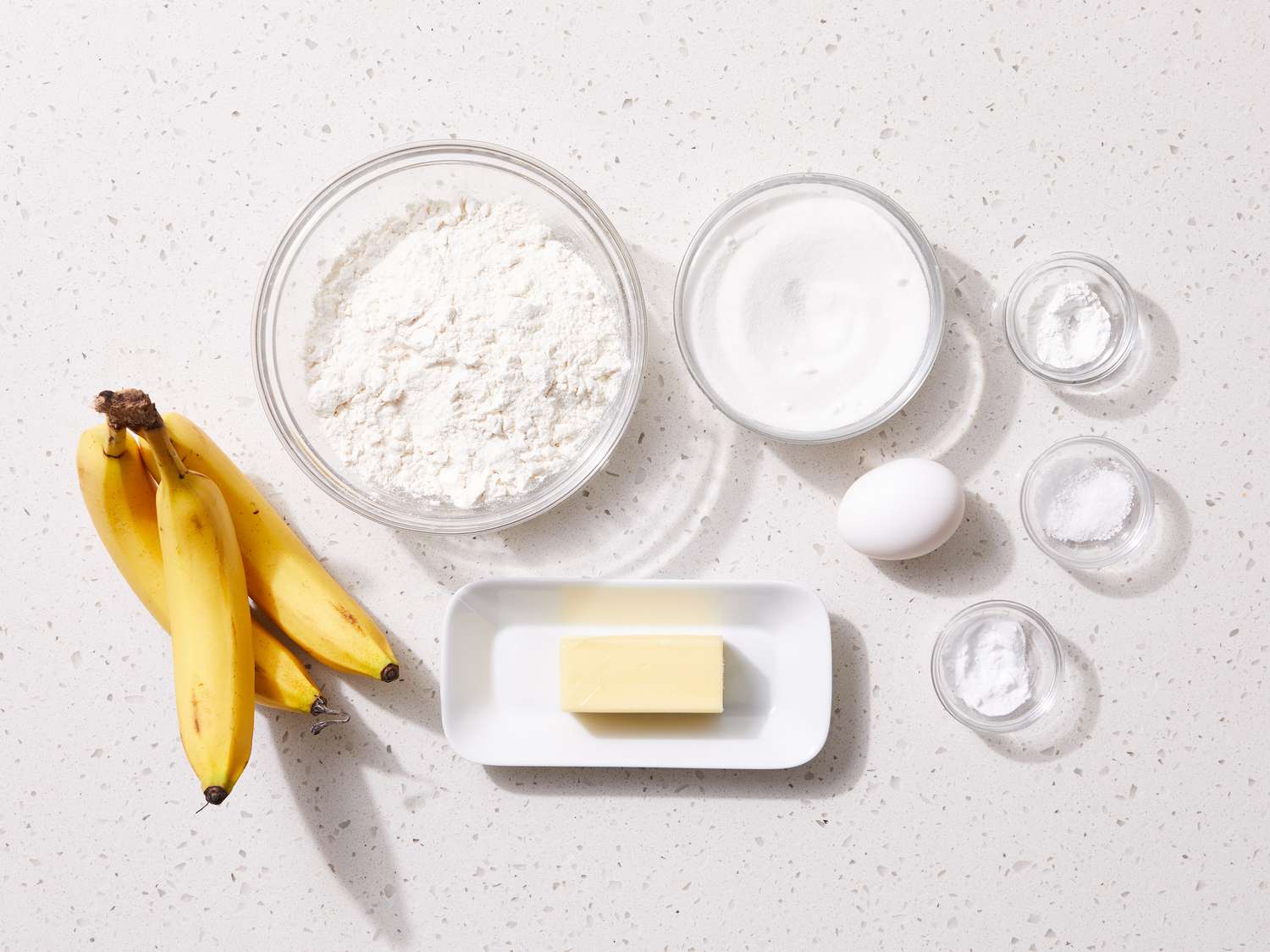 Measured ingredients for banana muffins arranged on a kitchen counter with ripe bananas, flour, brown sugar, butter, egg, and cinnamon