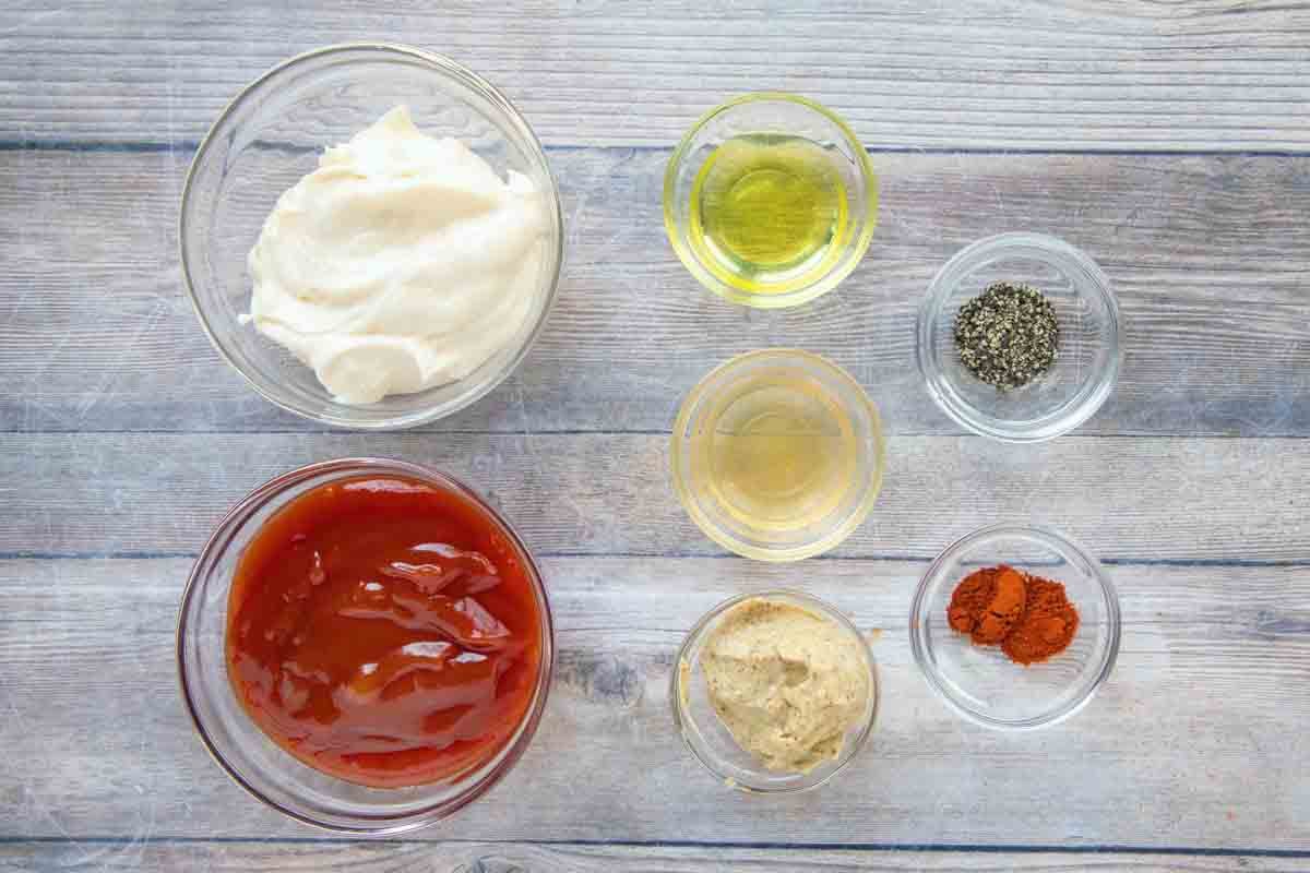 Measured ingredients for burger spread including mayonnaise, ketchup, dill pickles, sweet relish, vinegar, and spices arranged on a bright kitchen counter