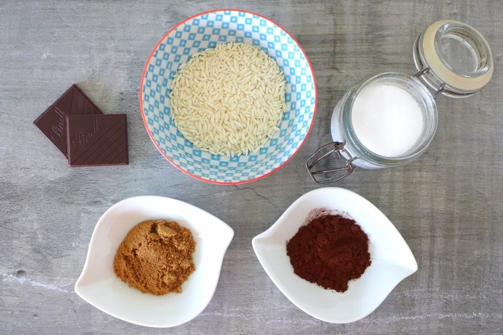 Measured ingredients for champorado on a kitchen counter including glutinous rice, unsweetened cocoa powder, sugar, salt, and a can of evaporated milk