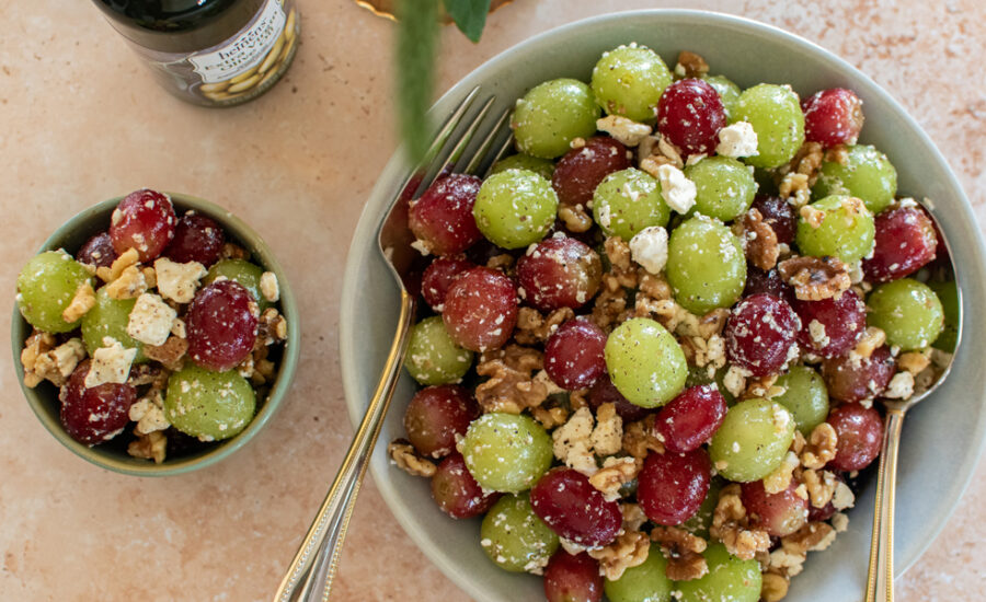 Measured ingredients for grape salad including bowls of red and green grapes, softened cream cheese, sour cream, vanilla, brown sugar, and chopped pecans on a tidy kitchen counter