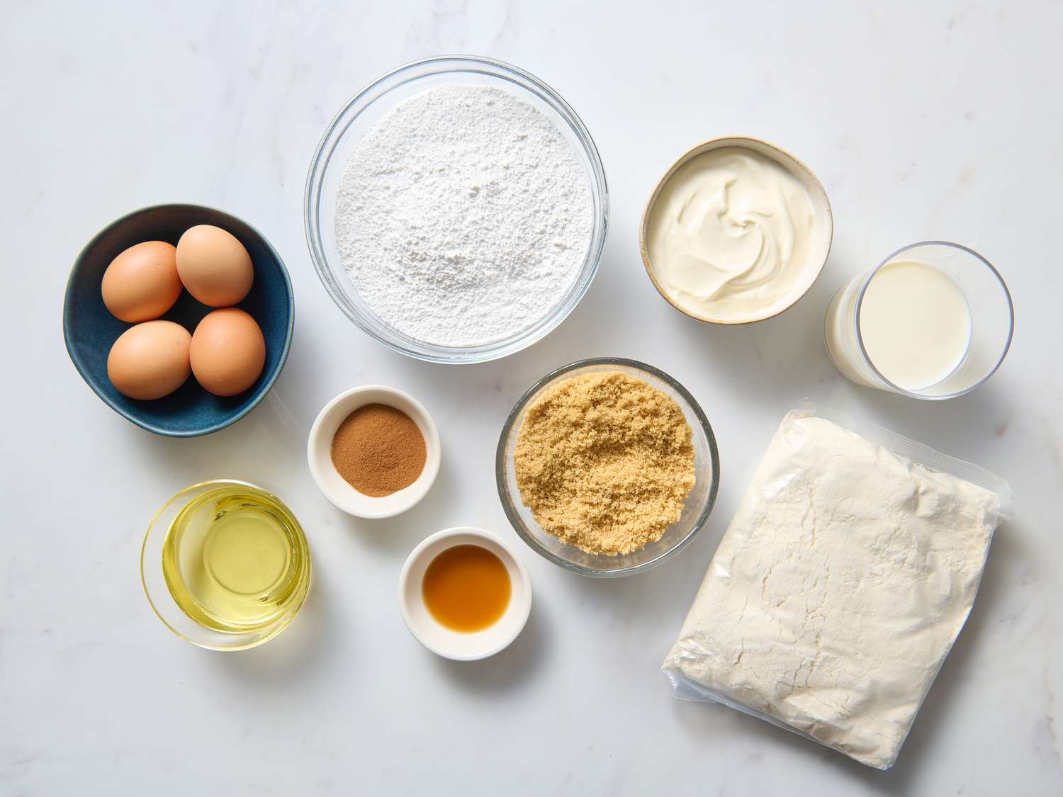 Measured ingredients for honey bun cake on a kitchen counter including flour, sugar, butter, eggs, sour cream, cinnamon, brown sugar, milk, and vanilla