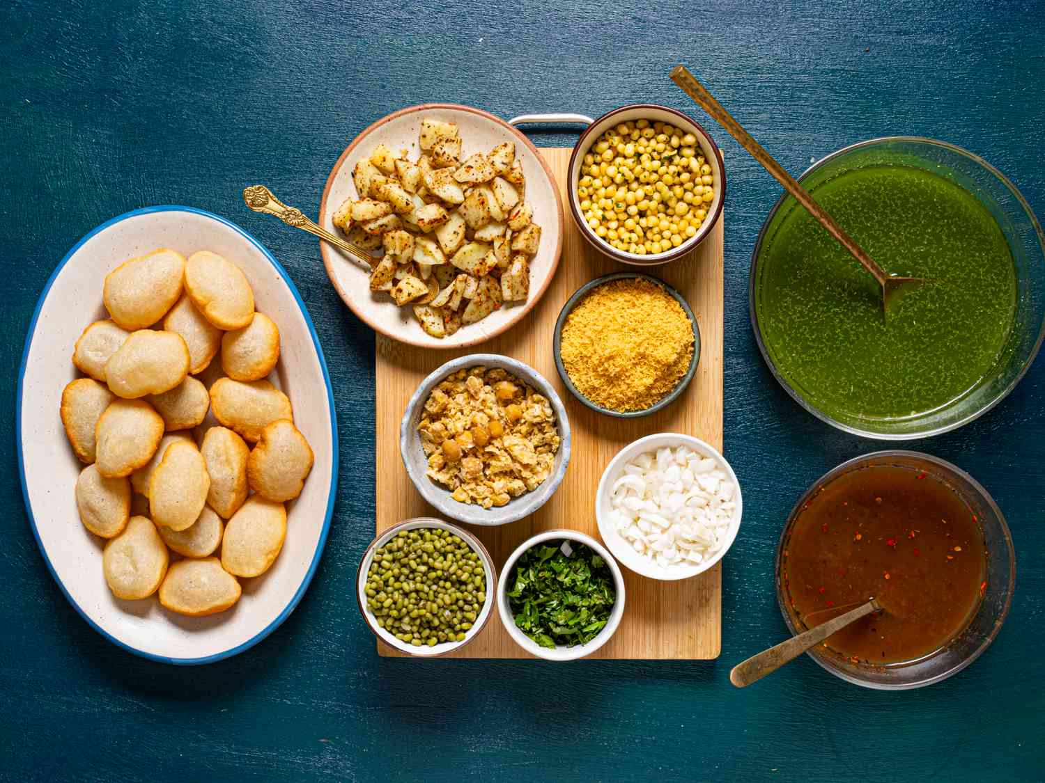 Measured ingredients for pani puri on a kitchen counter including puris, potatoes, chickpeas, mint, cilantro, green chilies, tamarind, spices, and lemons