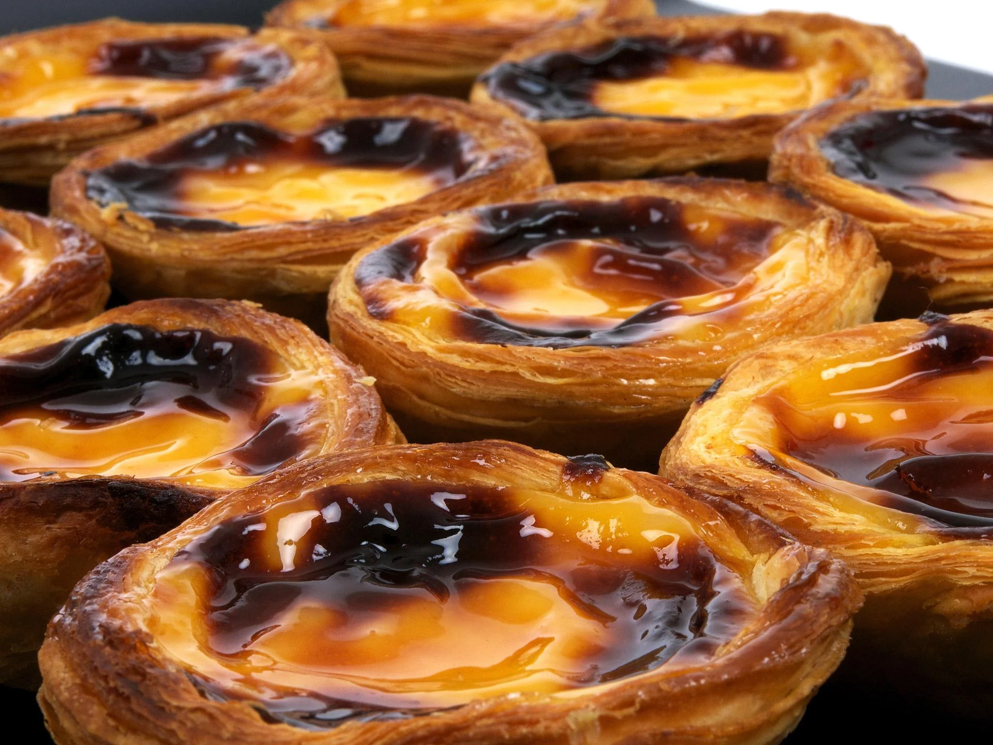 Measured ingredients for pastel de nata including milk, cream, sugar, egg yolks, cinnamon stick, lemon peel, and puff pastry on a bright kitchen counter