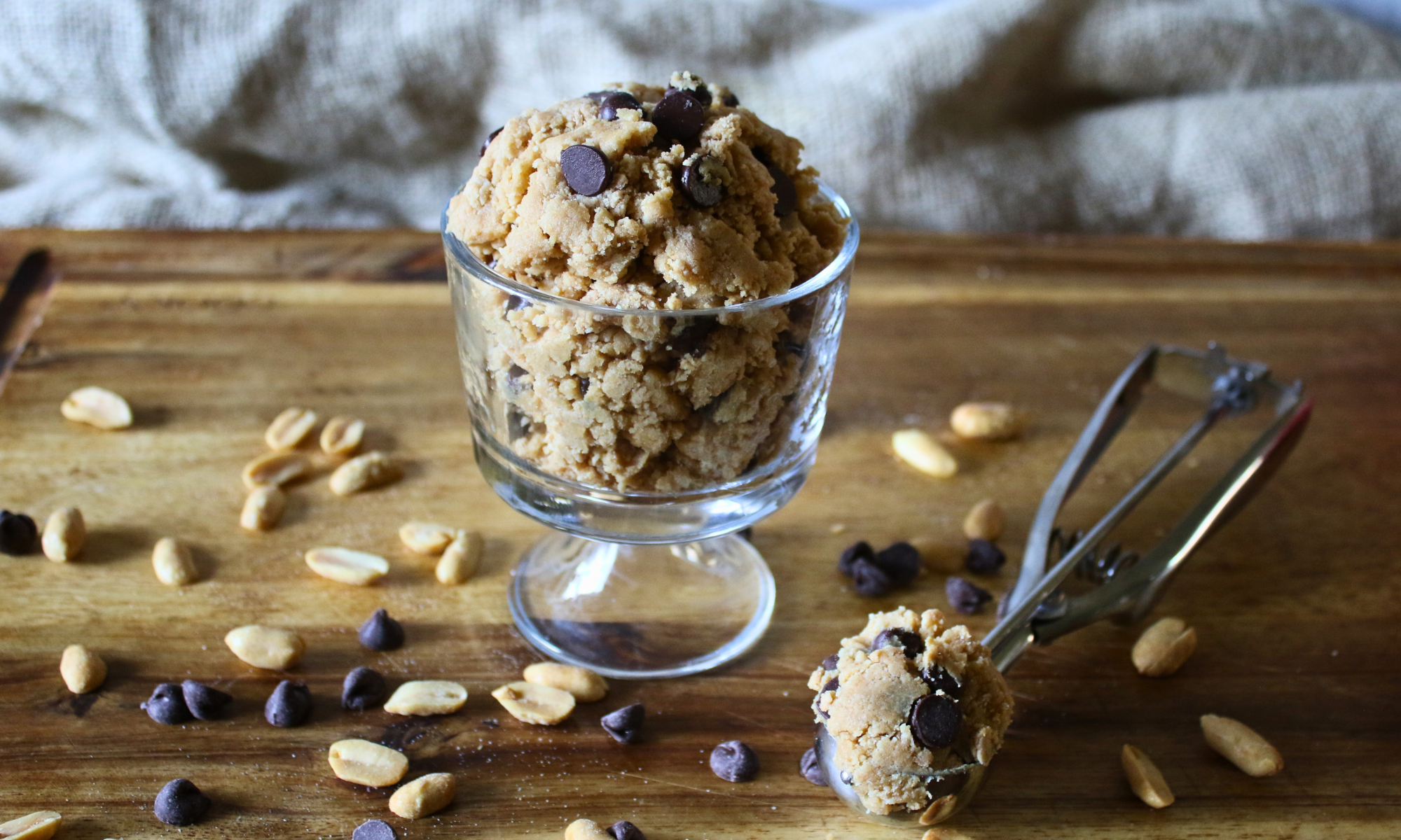 Measured ingredients for protein cookie dough on a kitchen counter including protein powder, almond flour, peanut butter, maple syrup, vanilla, milk, and mini chocolate chips in small bowls