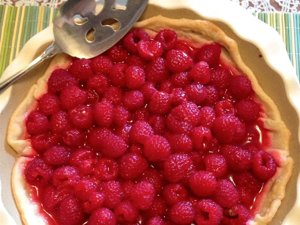 Measured ingredients for raspberry pie on a kitchen counter including raspberries, sugar, lemon, cornstarch, and pie crust dough