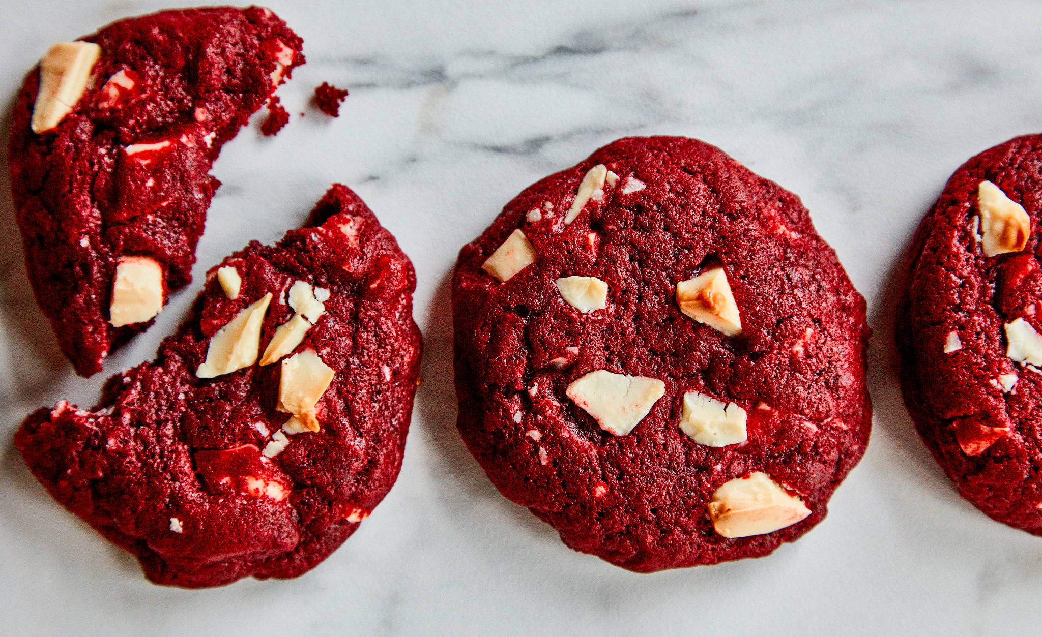Measured ingredients for red velvet cookies arranged on a clean kitchen counter including flour, cocoa powder, sugars, butter, eggs, vanilla, and red food coloring