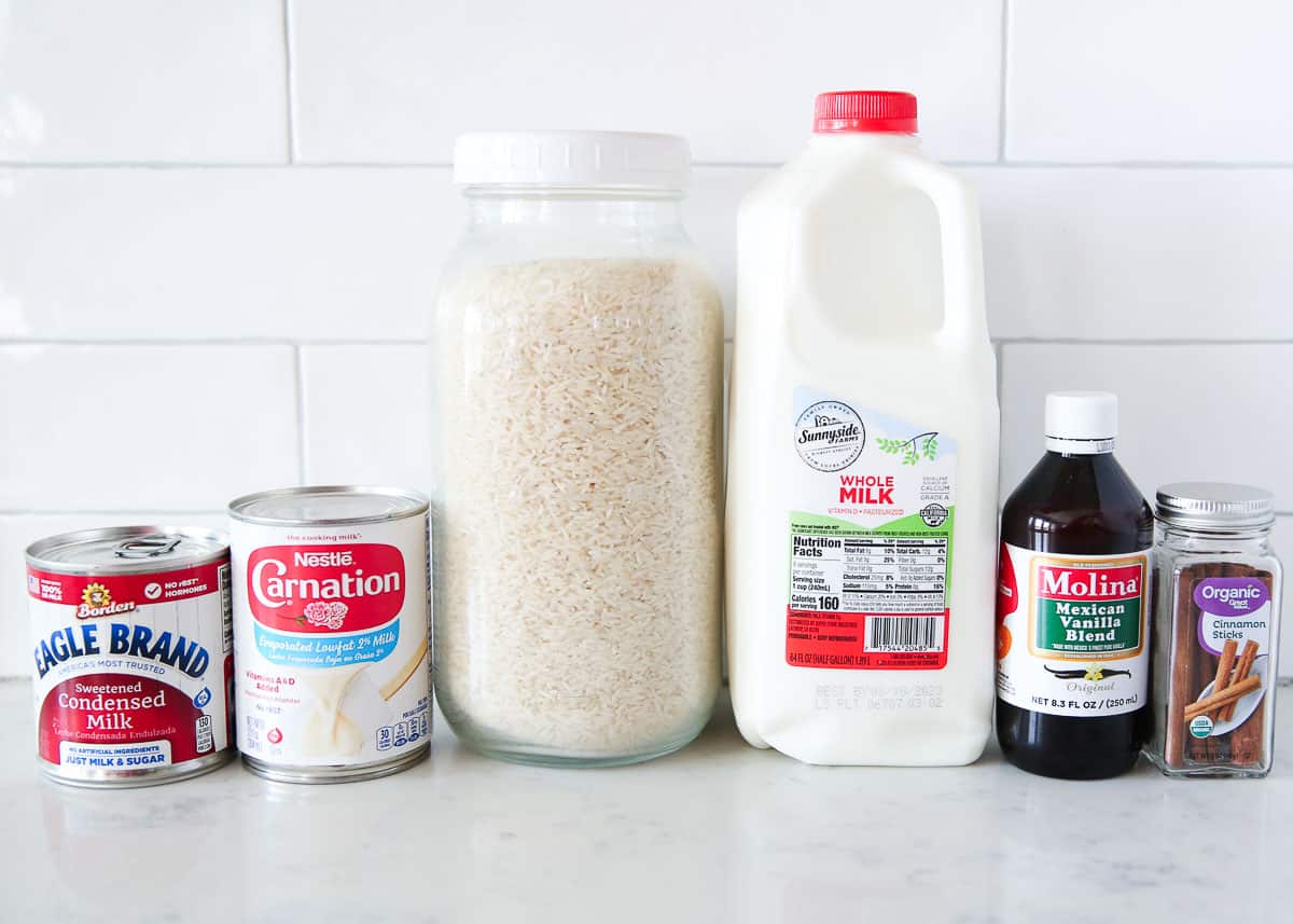 Measured ingredients for rice pudding including cooked rice, milk, sugar, cinnamon, vanilla, and salt arranged on a bright kitchen counter