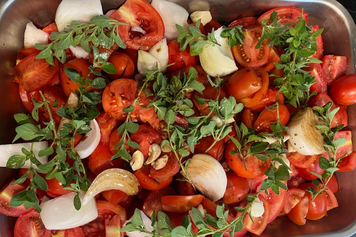 Measured ingredients for roasted tomato soup including fresh tomatoes, onion, garlic, olive oil, broth, basil, and seasonings on a tidy kitchen counter