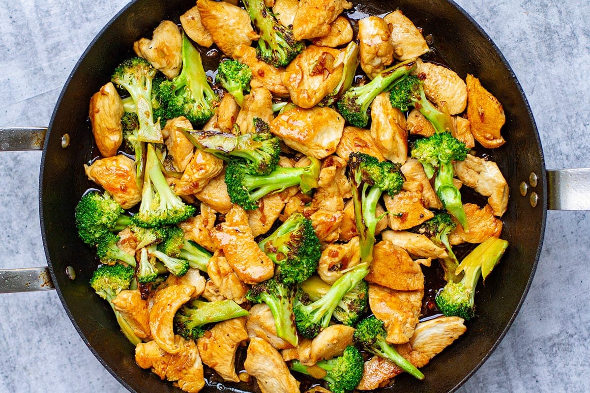 Measured ingredients for sesame-ginger chicken and broccoli on a kitchen counter, including soy sauce, honey, garlic, ginger, broccoli, and rice
