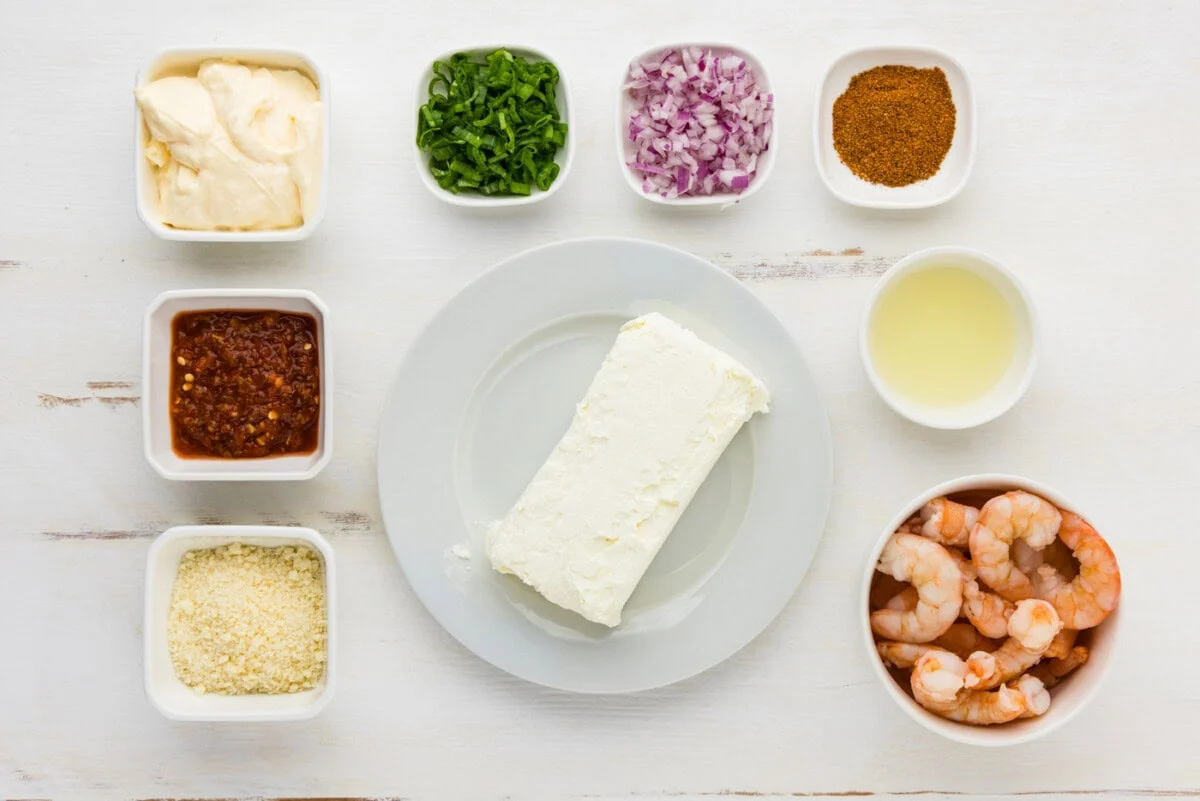 Measured ingredients for shrimp dip on a kitchen counter including cooked shrimp, cream cheese, sour cream, mayonnaise, lemon, scallions, dill, and seasonings